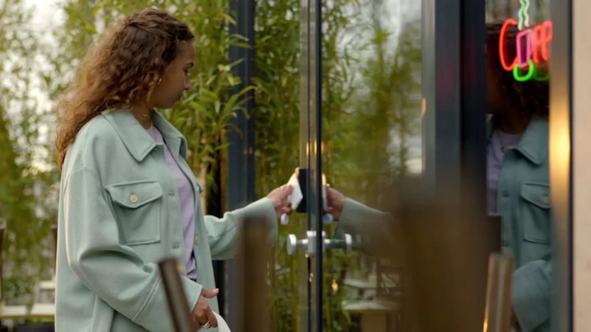A woman tapping a white access card on a reader to unlock a glass storefront door