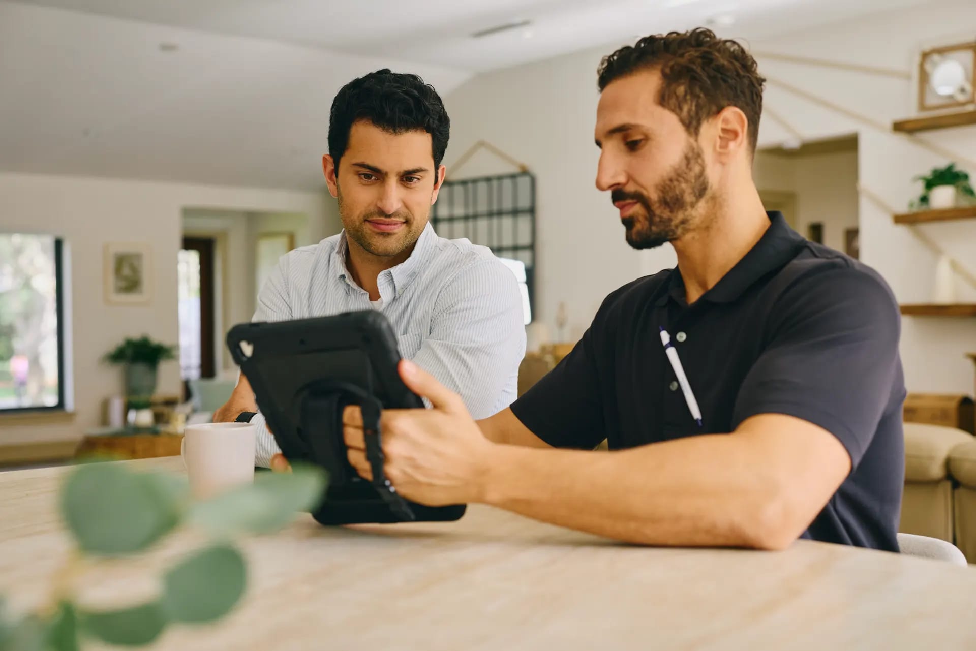 Two men reviewing home security options together on a tablet at a kitchen table