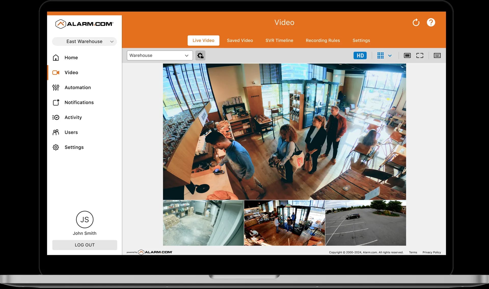 The Alarm.com commercial video monitoring dashboard displaying a multi-camera grid of a café interior alongside a single enlarged camera feed