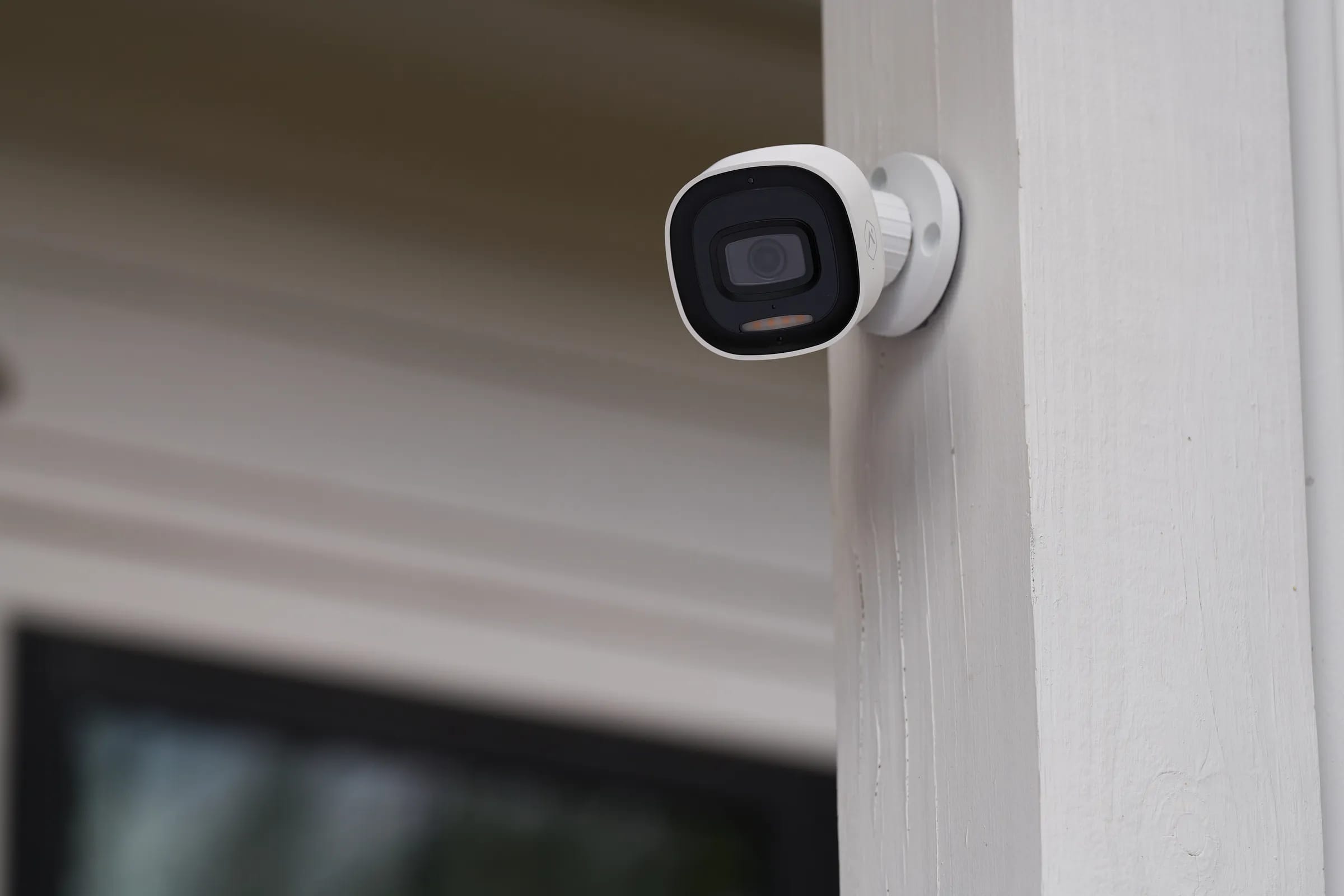 A white bullet security camera mounted on the exterior trim of a home