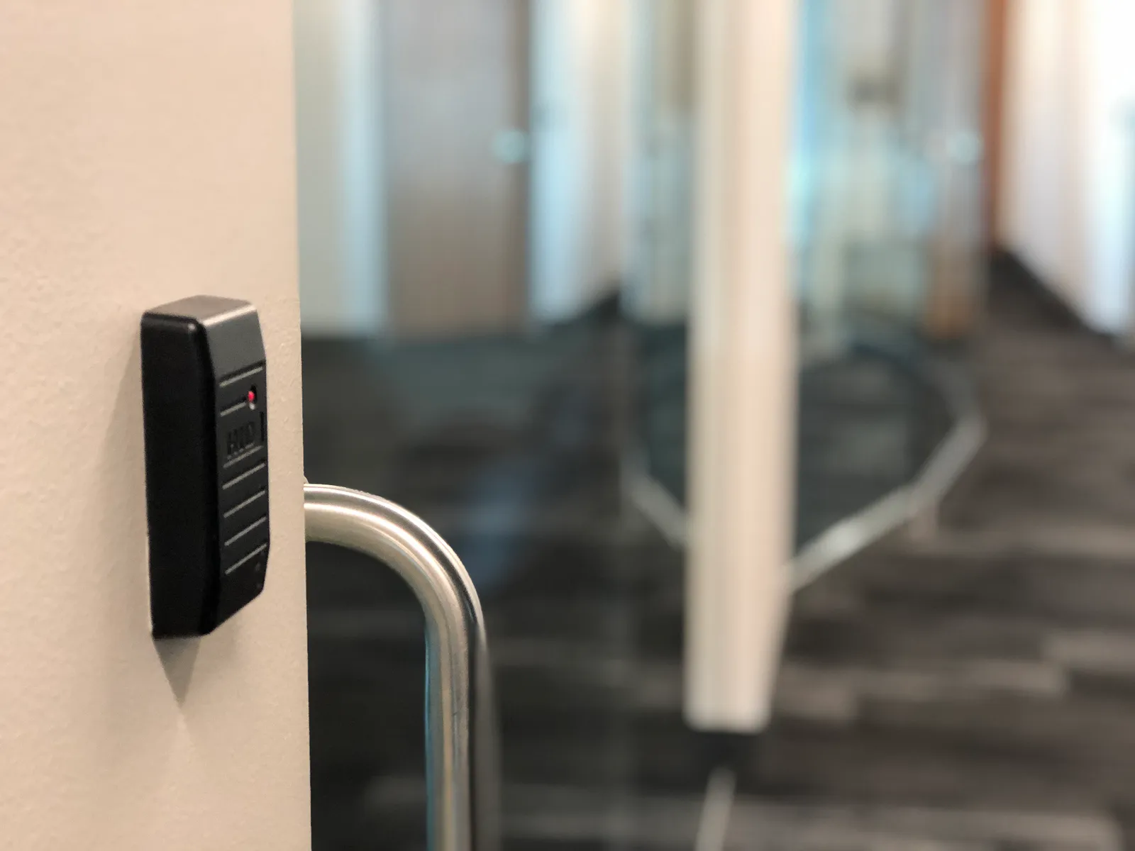 A black keypad card reader mounted on the wall beside a glass office door