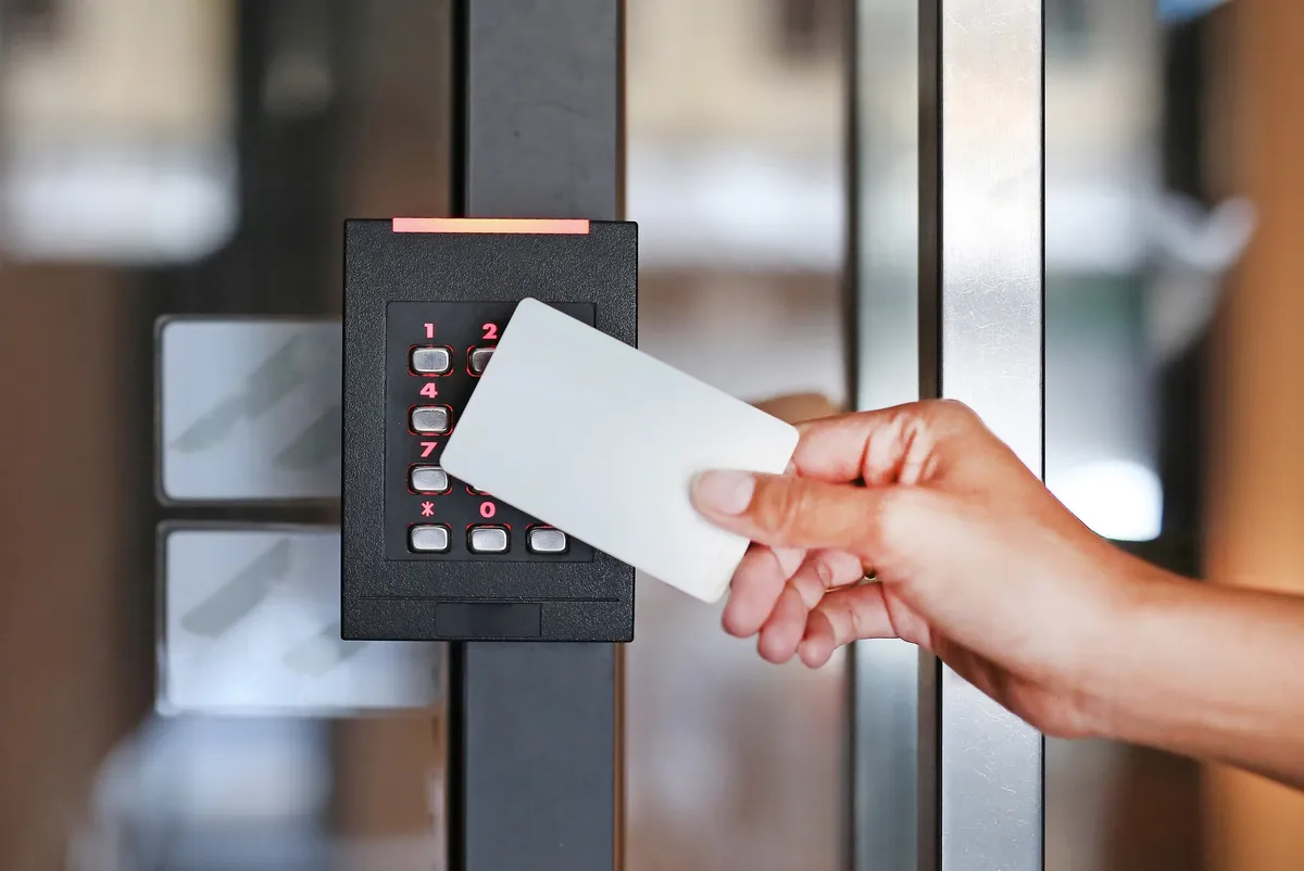 A hand holding an access card up to a keypad card reader to unlock a glass office door