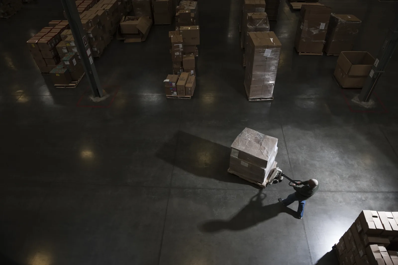 Warehouse worker using a manual pallet jack to move stacked goods in a secured commercial facility