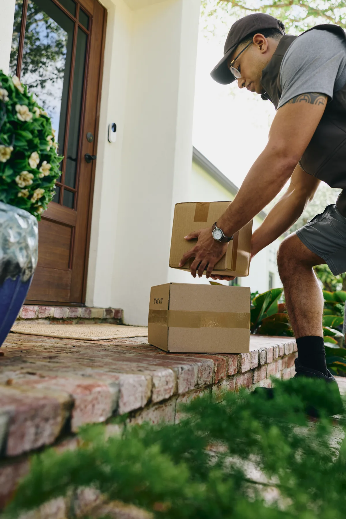 Delivery driver placing packages on a customer's doorstep beneath a video doorbell camera