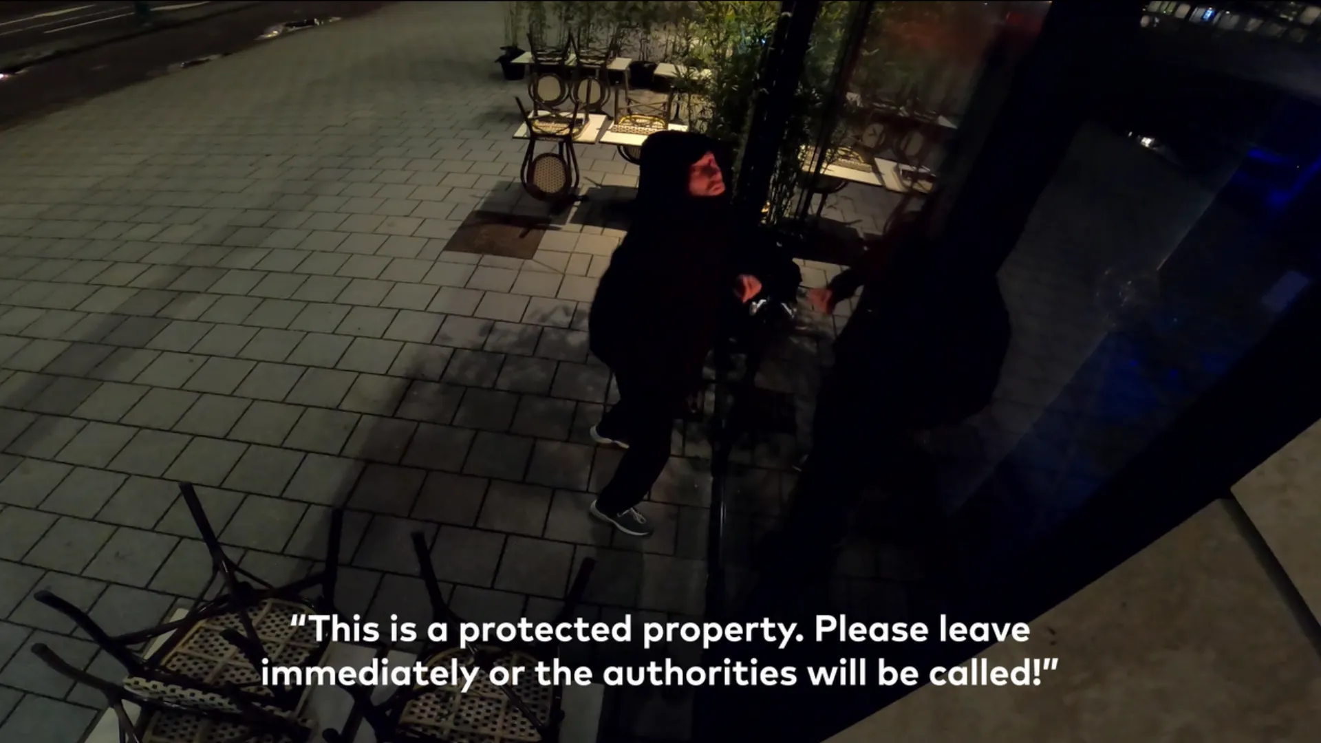 Night security camera still of a hooded intruder at a storefront, overlaid with the live voice-down caption: "This is a protected property. Please leave immediately or the authorities will be called!"