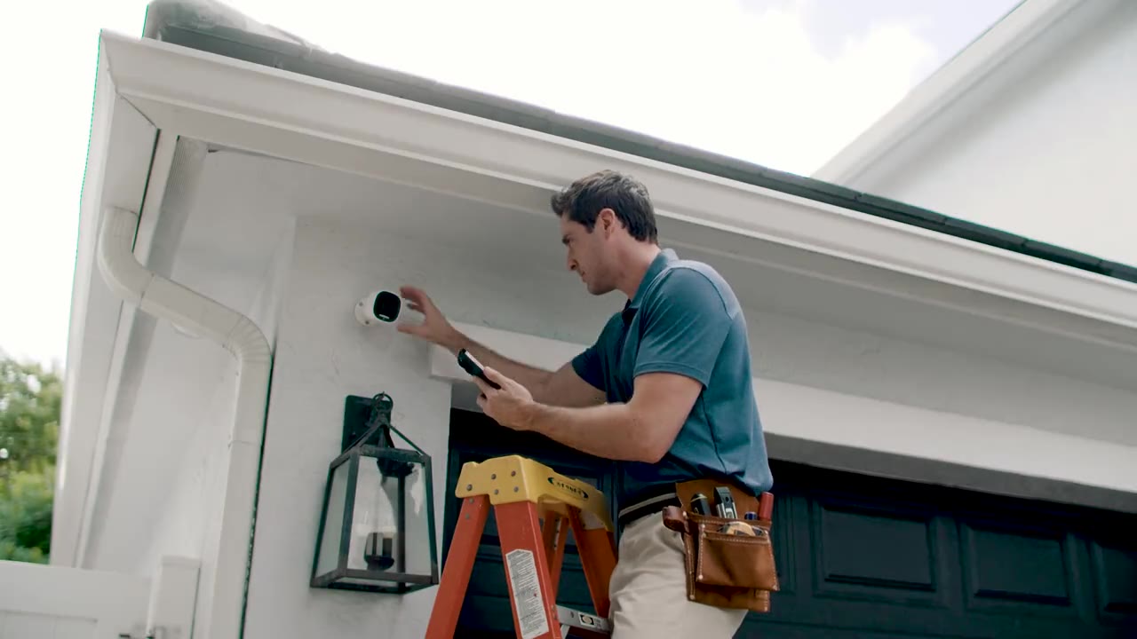 Technician on a ladder installing an outdoor security camera under the eaves of a residential home