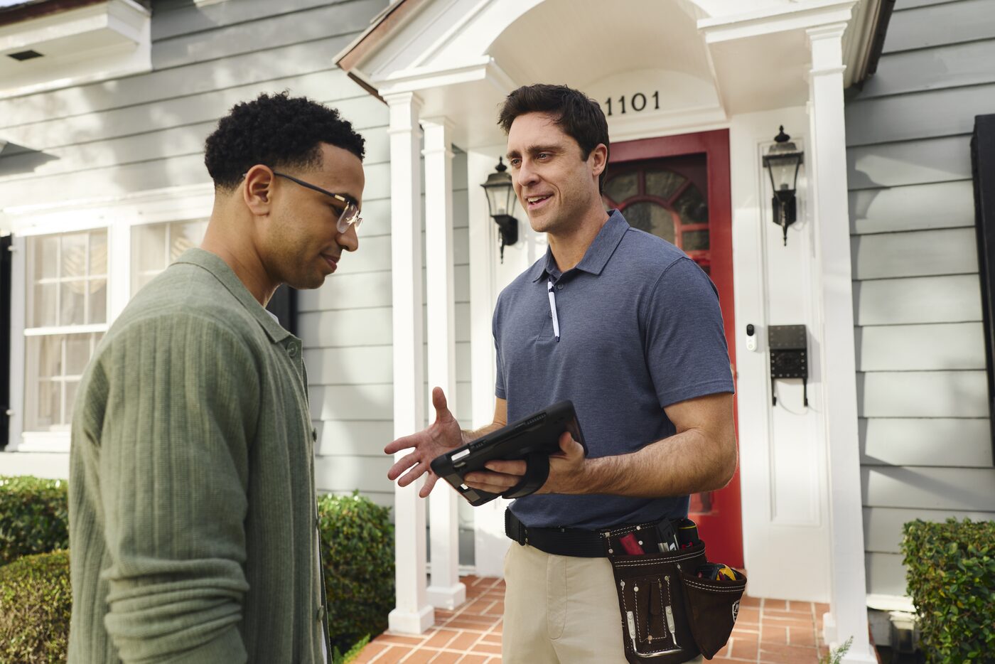 A Security ONE technician reviewing a home security plan on a tablet with a homeowner at their front door