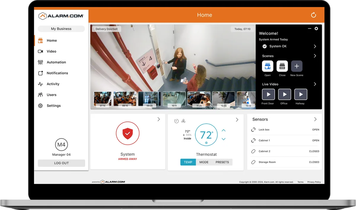 The Alarm.com commercial dashboard shown on a laptop with live video of a stairwell, thermostat controls, and door sensor statuses